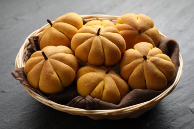 Photo of Wicker basket with tasty pumpkin shaped buns on dark textured table, closeup