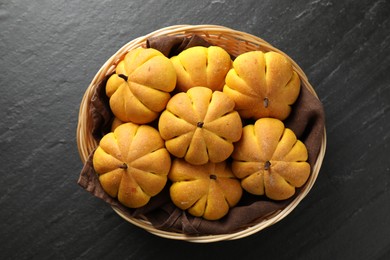 Photo of Wicker basket with tasty pumpkin shaped buns on dark textured table, top view