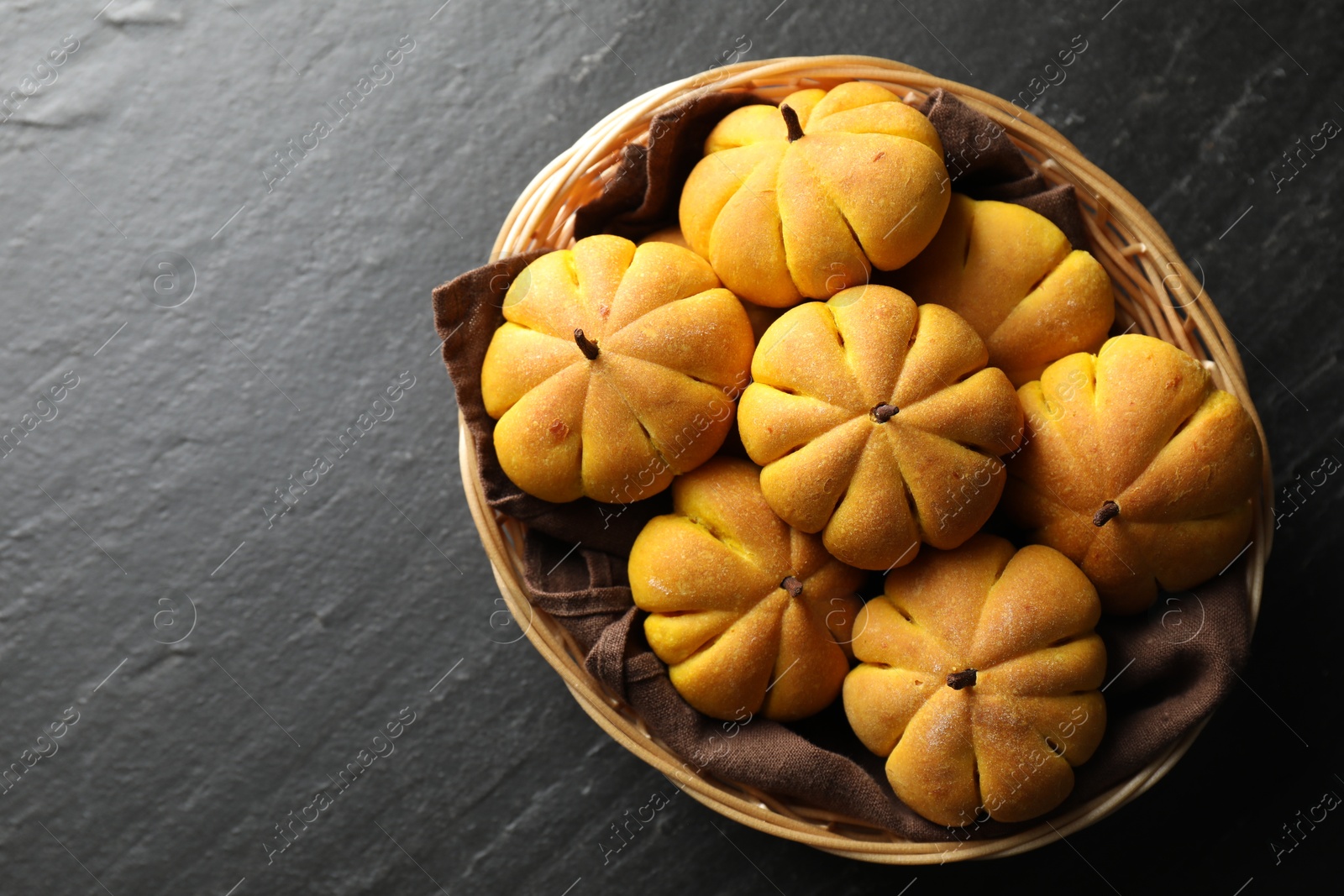 Photo of Wicker basket with tasty pumpkin shaped buns on dark textured table, top view. Space for text