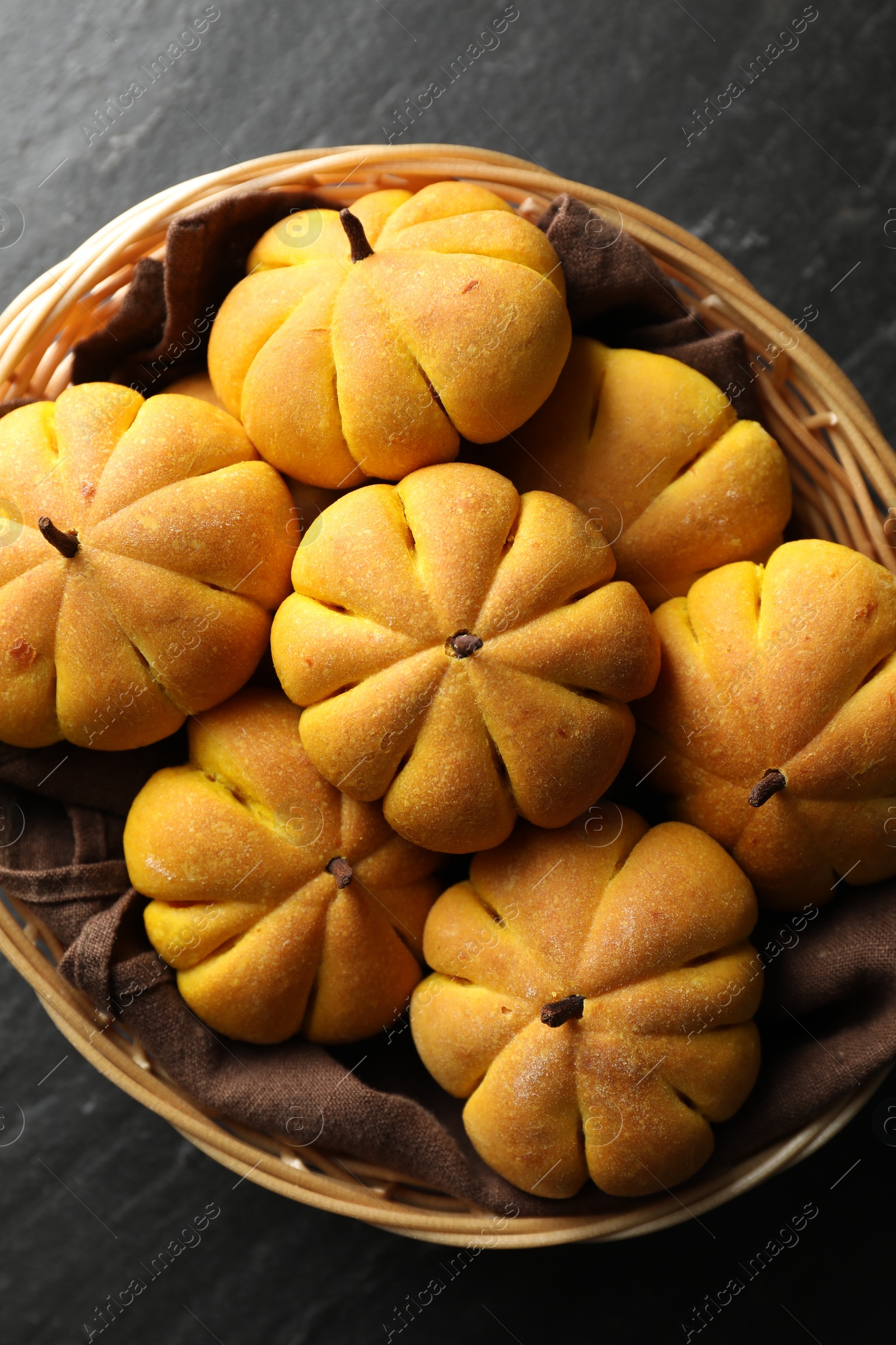 Photo of Wicker basket with tasty pumpkin shaped buns on dark textured table, top view