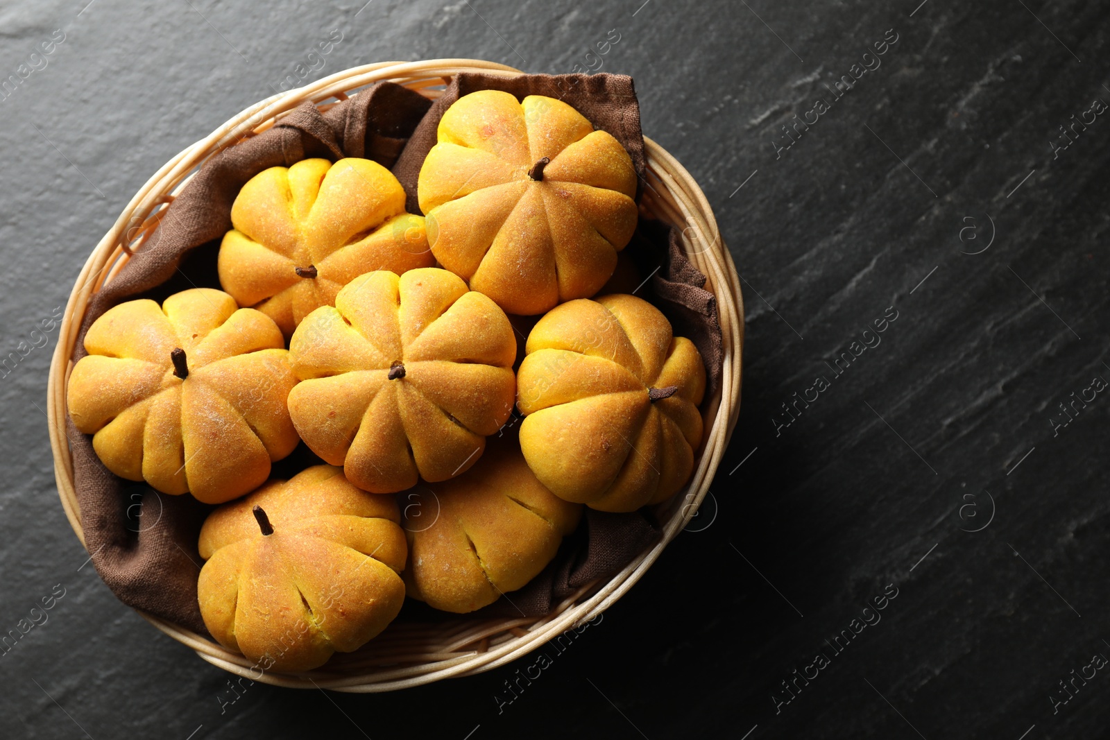 Photo of Wicker basket with tasty pumpkin shaped buns on dark textured table, top view. Space for text