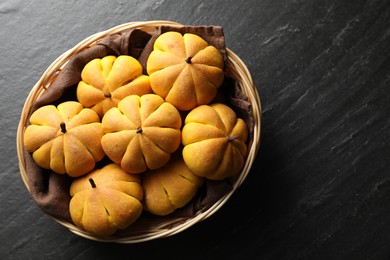 Photo of Wicker basket with tasty pumpkin shaped buns on dark textured table, top view. Space for text