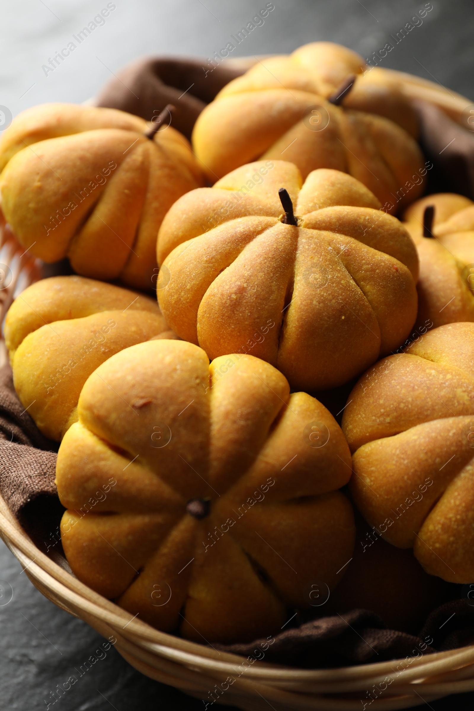 Photo of Wicker basket with tasty pumpkin shaped buns on dark table, closeup