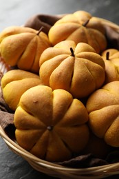 Photo of Wicker basket with tasty pumpkin shaped buns on dark table, closeup