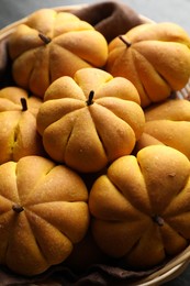 Photo of Tasty pumpkin shaped buns in wicker basket, closeup