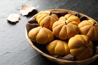 Photo of Wicker basket with tasty pumpkin shaped buns on dark textured table, closeup. Space for text