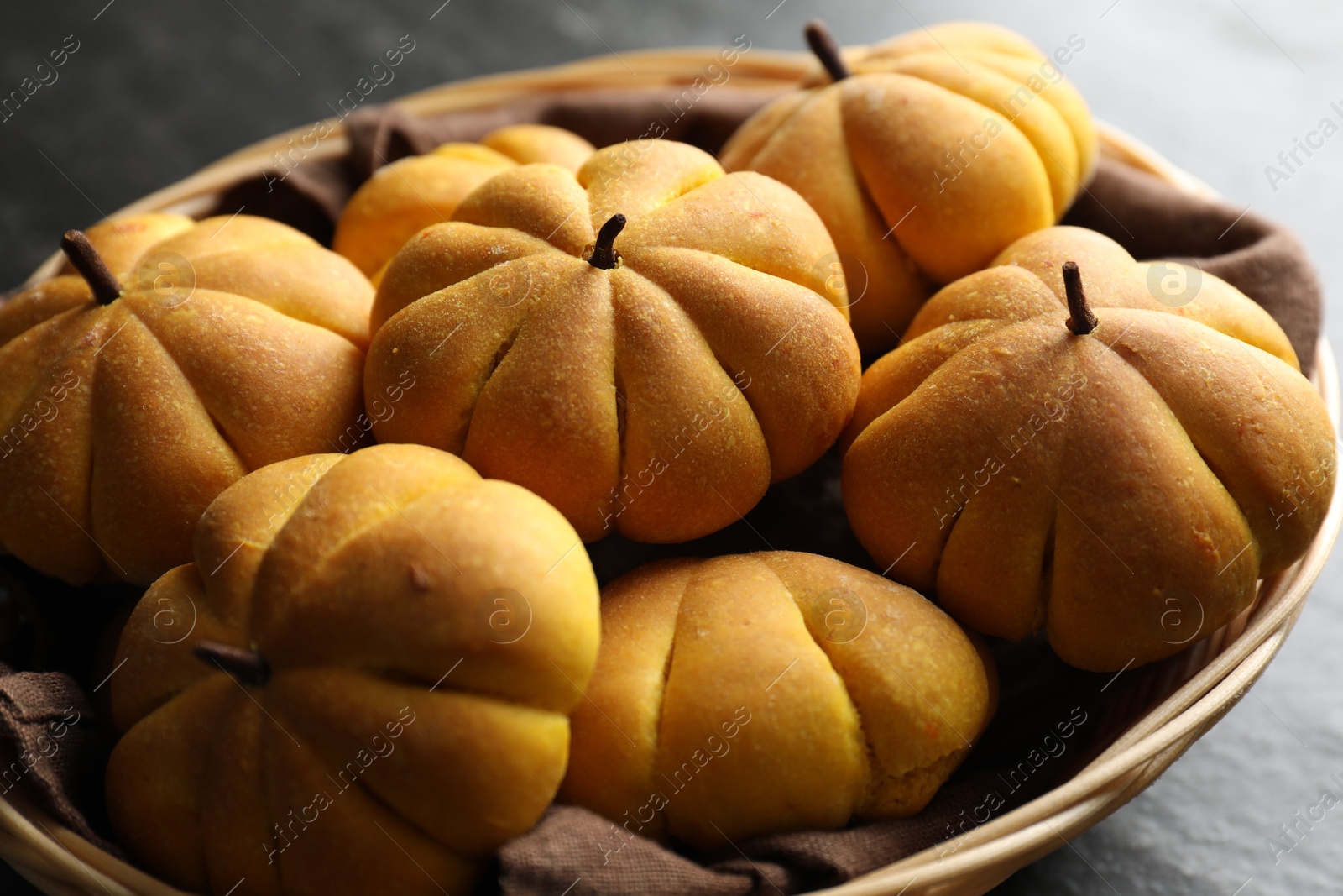 Photo of Wicker basket with tasty pumpkin shaped buns on dark table, closeup