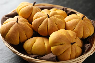 Photo of Wicker basket with tasty pumpkin shaped buns on dark table, closeup