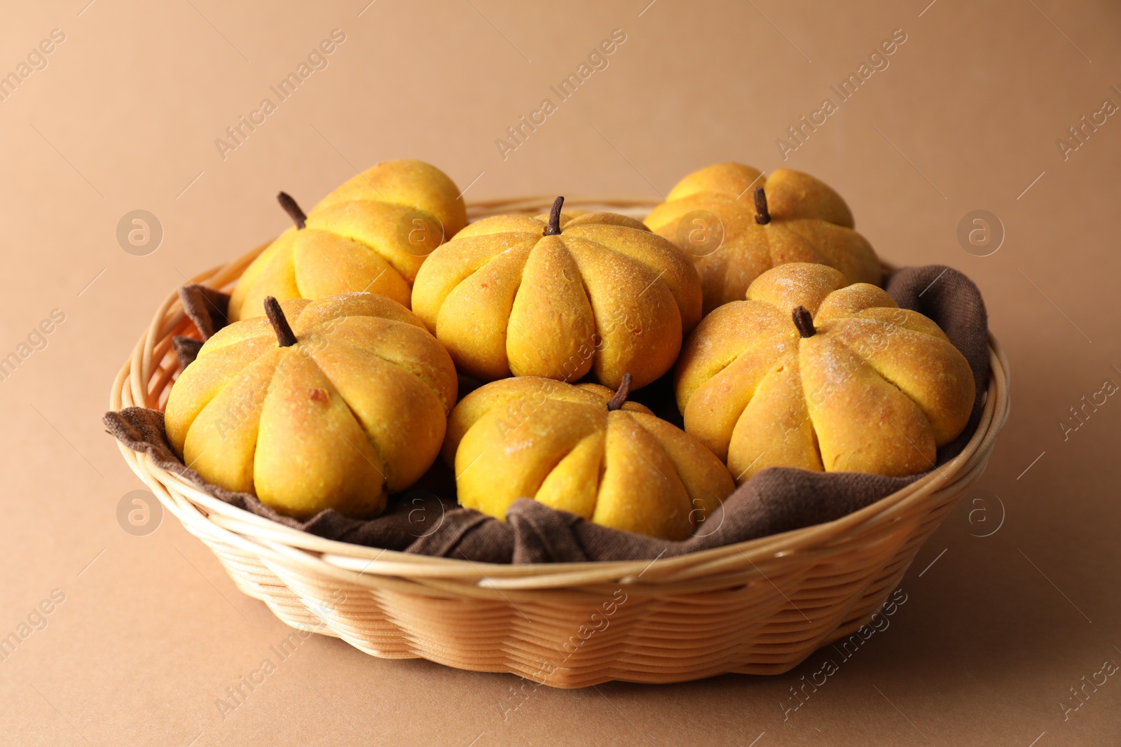 Photo of Wicker basket with tasty pumpkin shaped buns on beige background, closeup