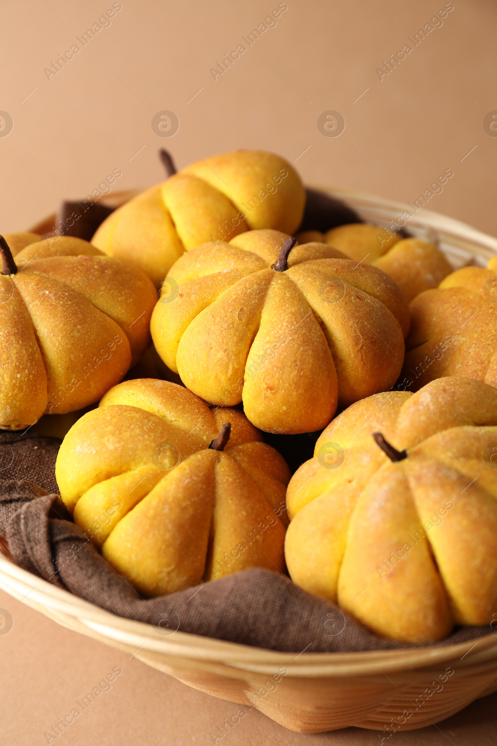 Photo of Wicker basket with tasty pumpkin shaped buns on beige background, closeup