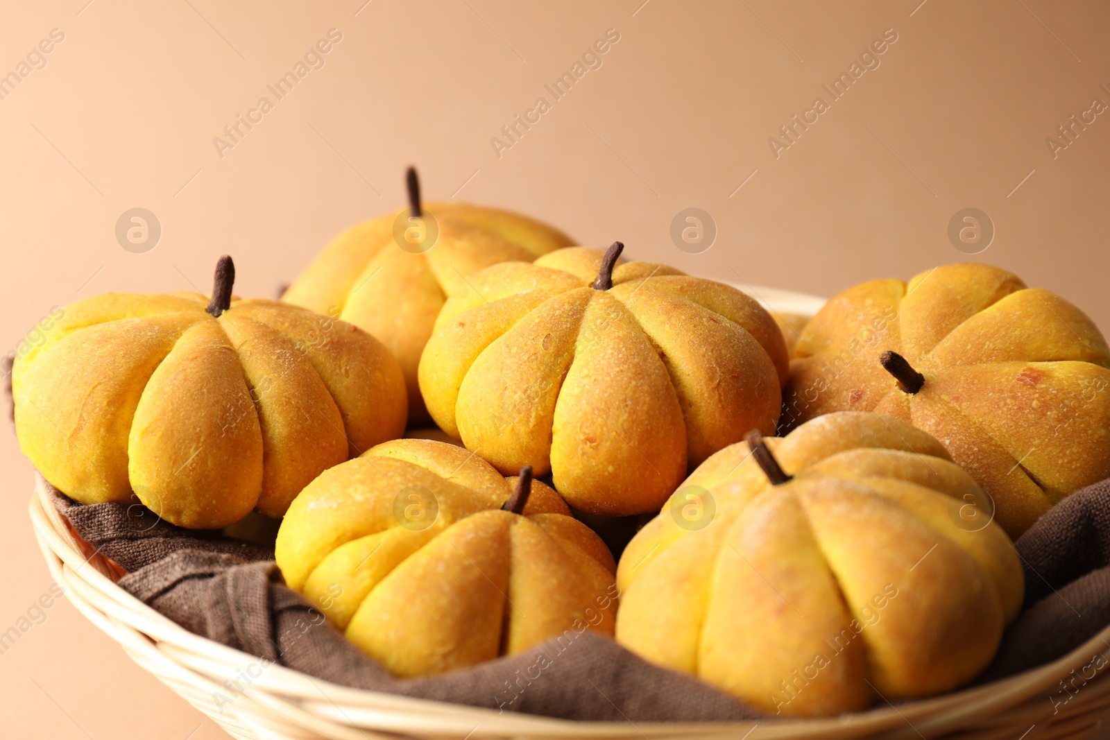 Photo of Wicker basket with tasty pumpkin shaped buns on beige background, closeup