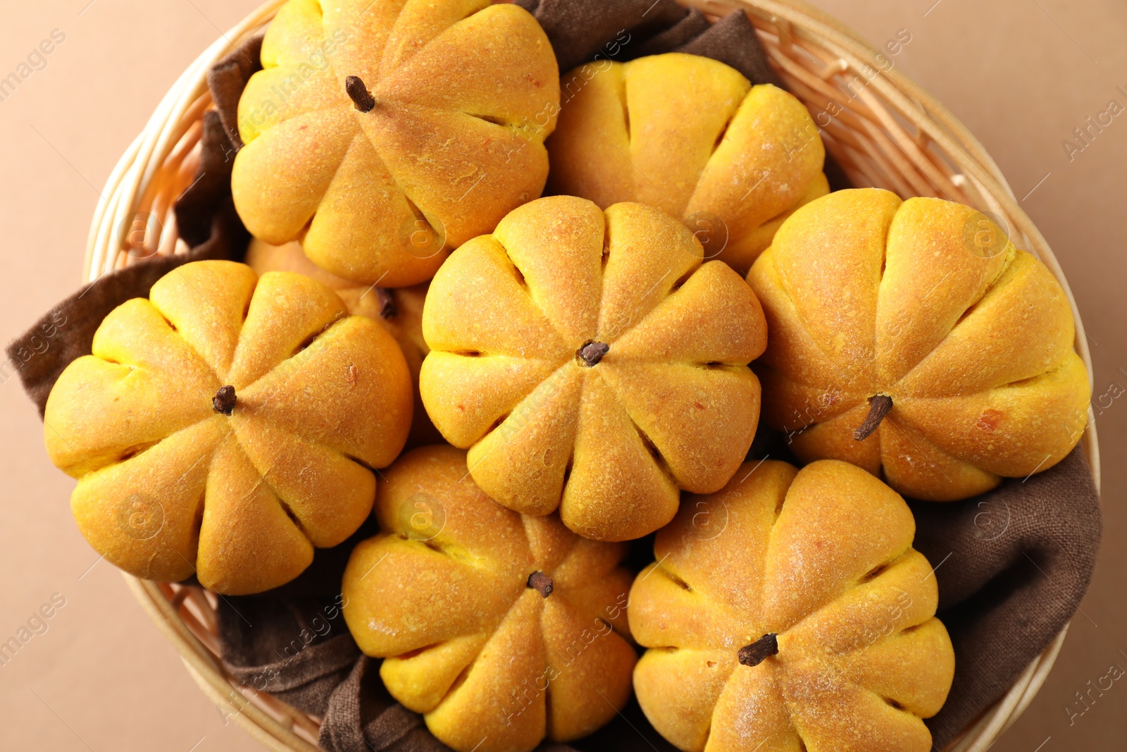 Photo of Wicker basket with tasty pumpkin shaped buns on beige background, top view