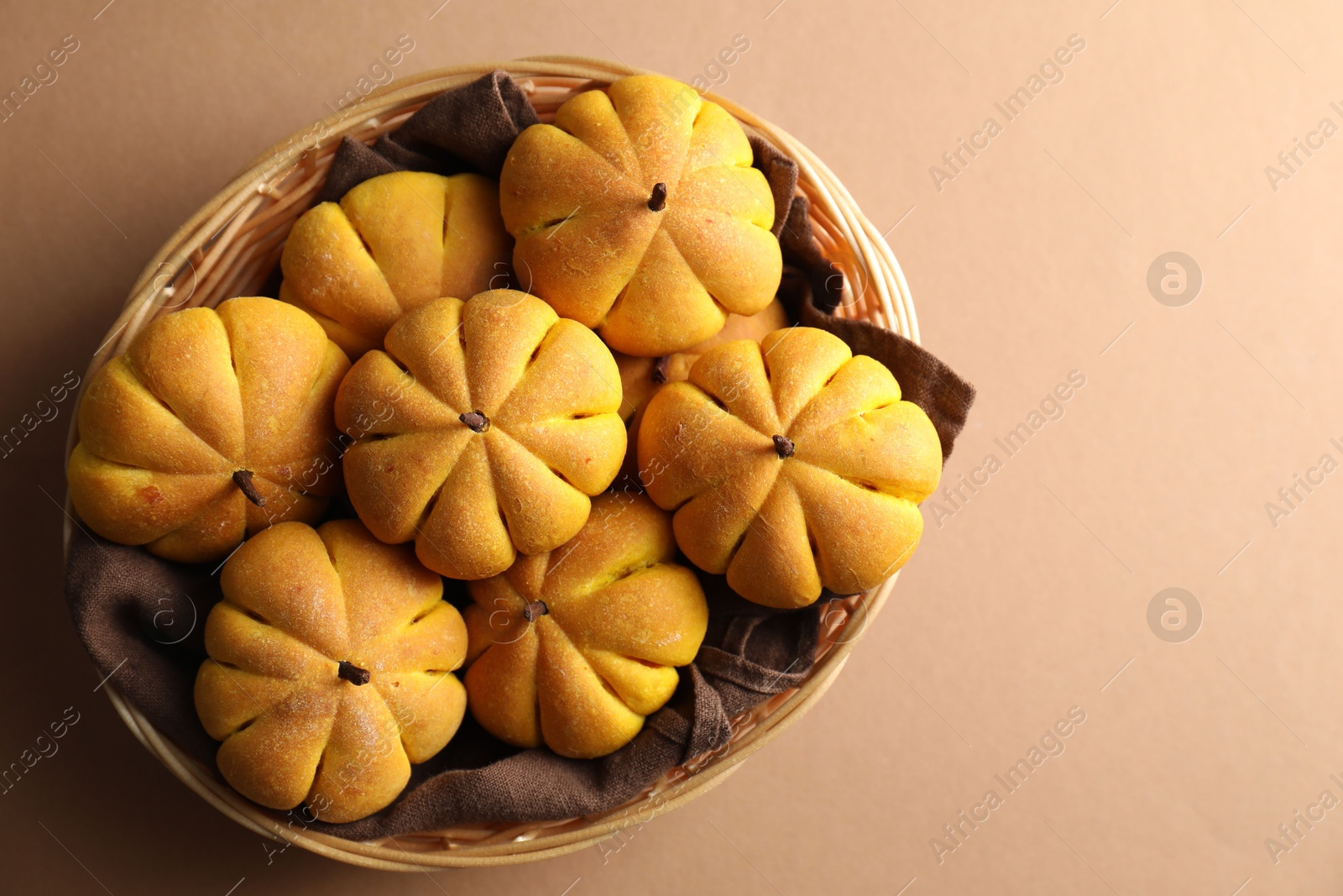 Photo of Wicker basket with tasty pumpkin shaped buns on beige background, top view. Space for text