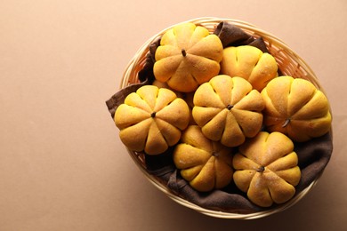 Photo of Wicker basket with tasty pumpkin shaped buns on beige background, top view. Space for text