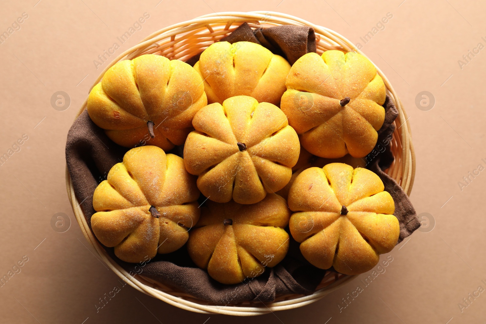 Photo of Wicker basket with tasty pumpkin shaped buns on beige background, top view