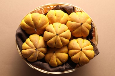 Photo of Wicker basket with tasty pumpkin shaped buns on beige background, top view