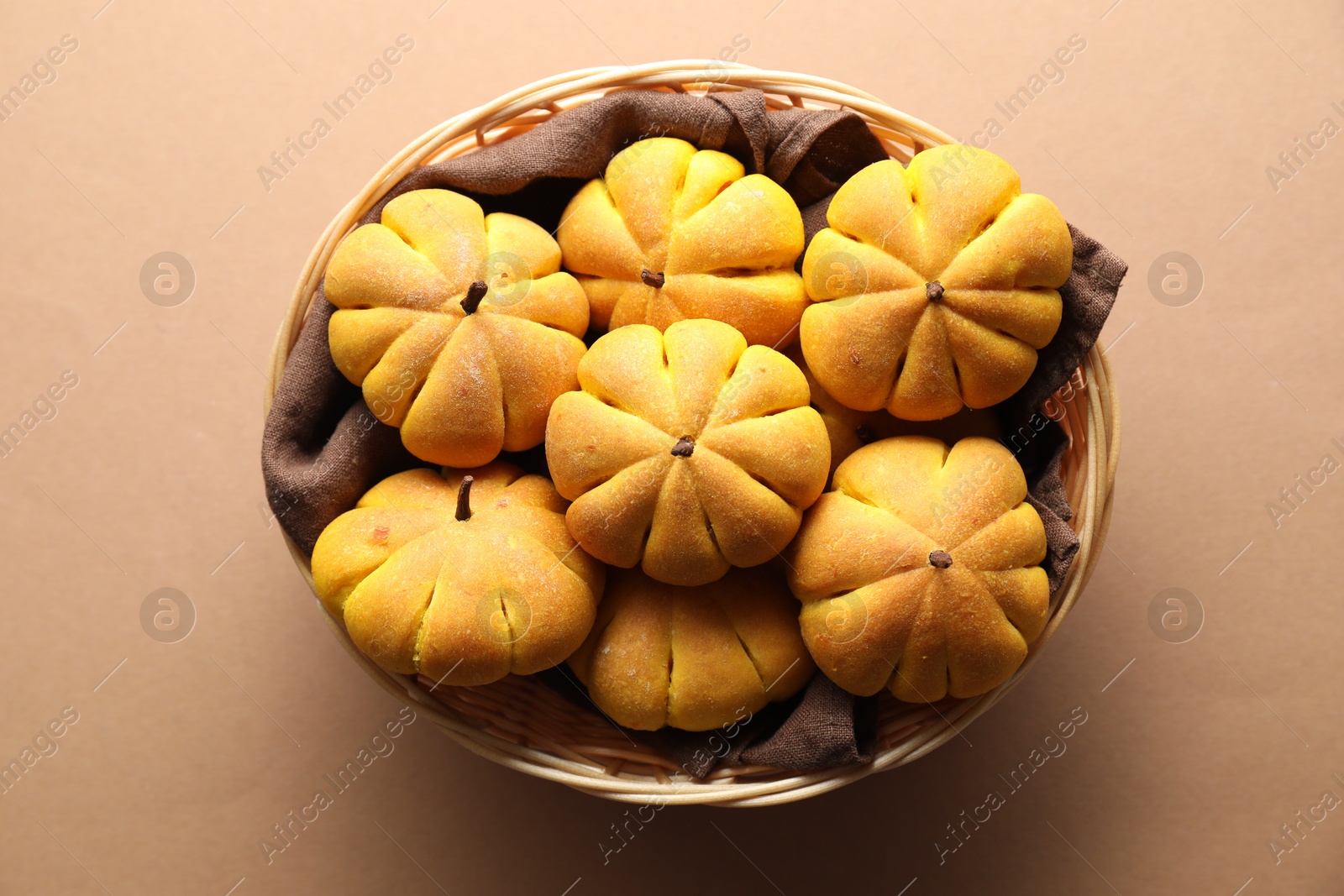 Photo of Wicker basket with tasty pumpkin shaped buns on beige background, top view