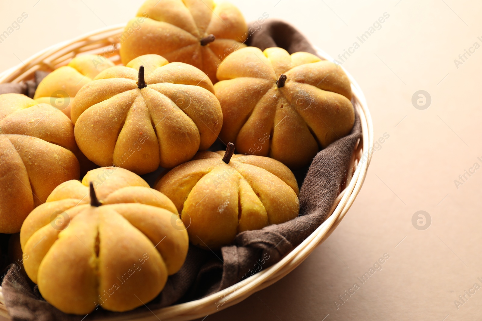 Photo of Wicker basket with tasty pumpkin shaped buns on beige background, closeup