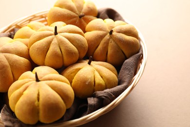 Photo of Wicker basket with tasty pumpkin shaped buns on beige background, closeup