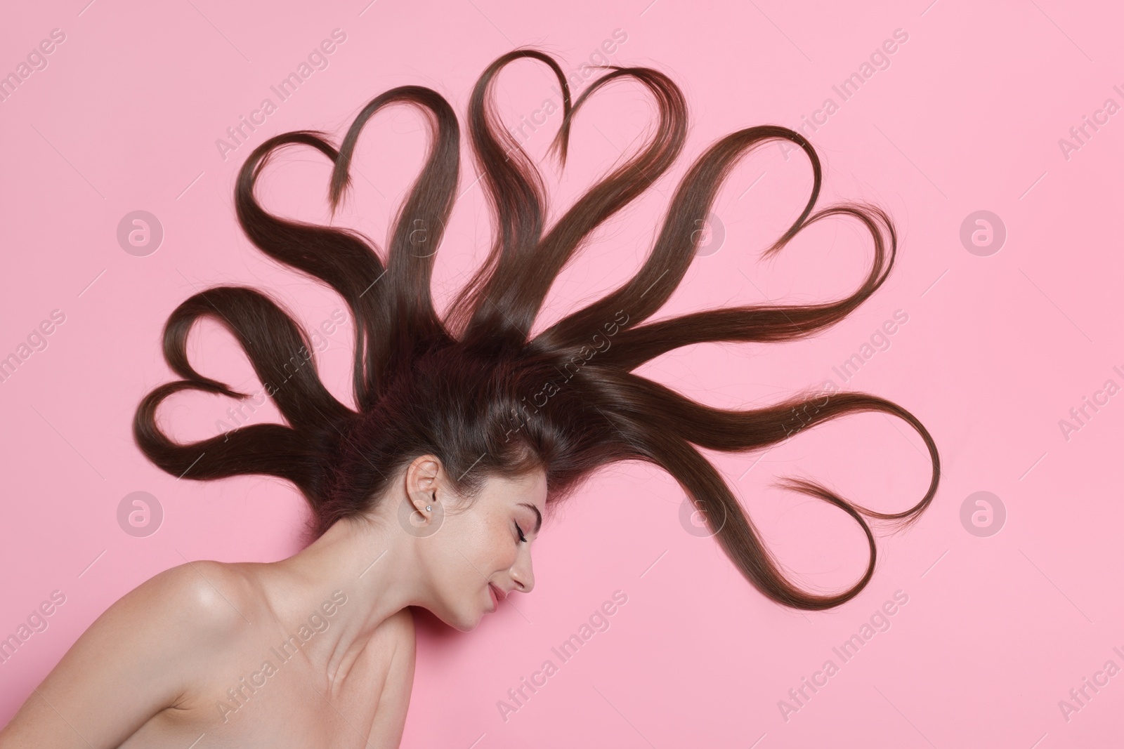 Photo of Beautiful young woman with hair in shape of hearts on pink background, top view