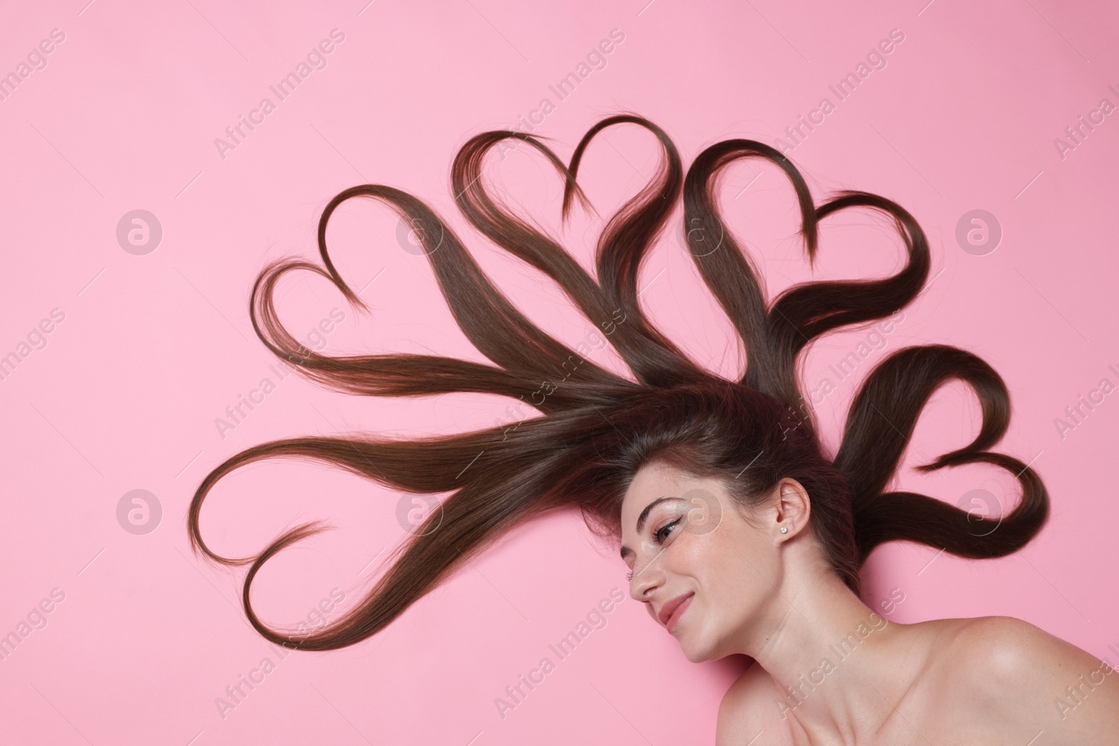 Photo of Beautiful young woman with hair in shape of hearts on pink background, top view