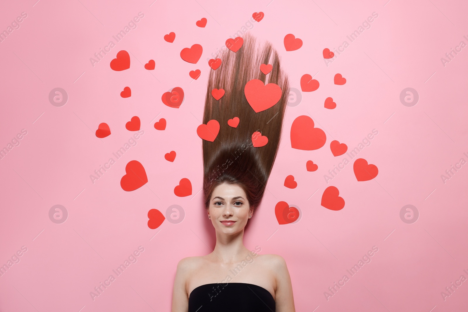 Photo of Beautiful young woman with long hair and red paper hearts on pink background, top view