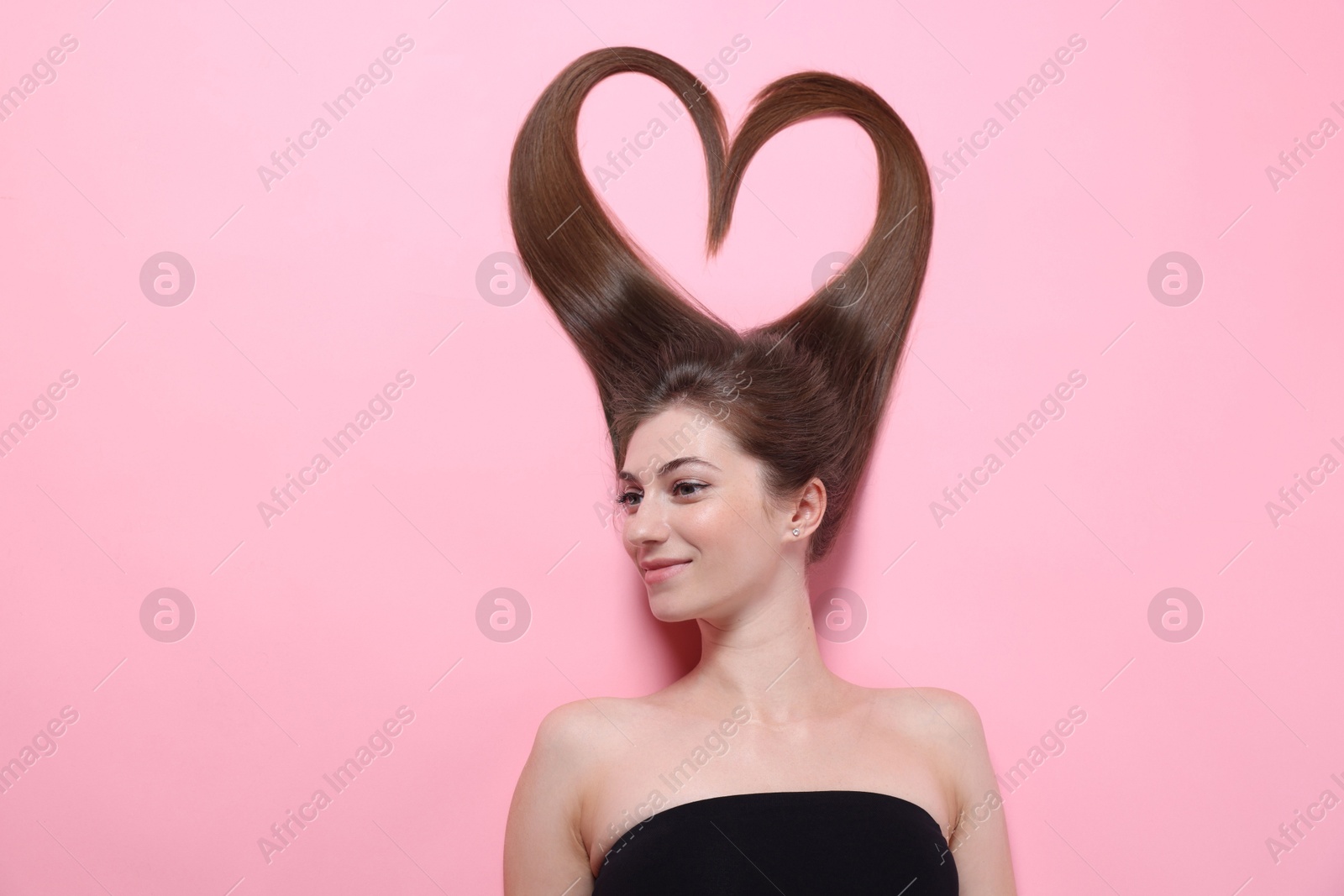 Photo of Beautiful young woman with hair in shape of heart on pink background, top view