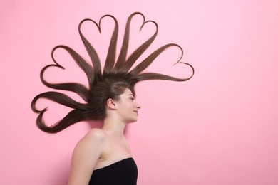 Photo of Beautiful young woman with hair in shape of hearts on pink background, top view. Space for text