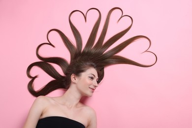 Photo of Beautiful young woman with hair in shape of hearts on pink background, top view