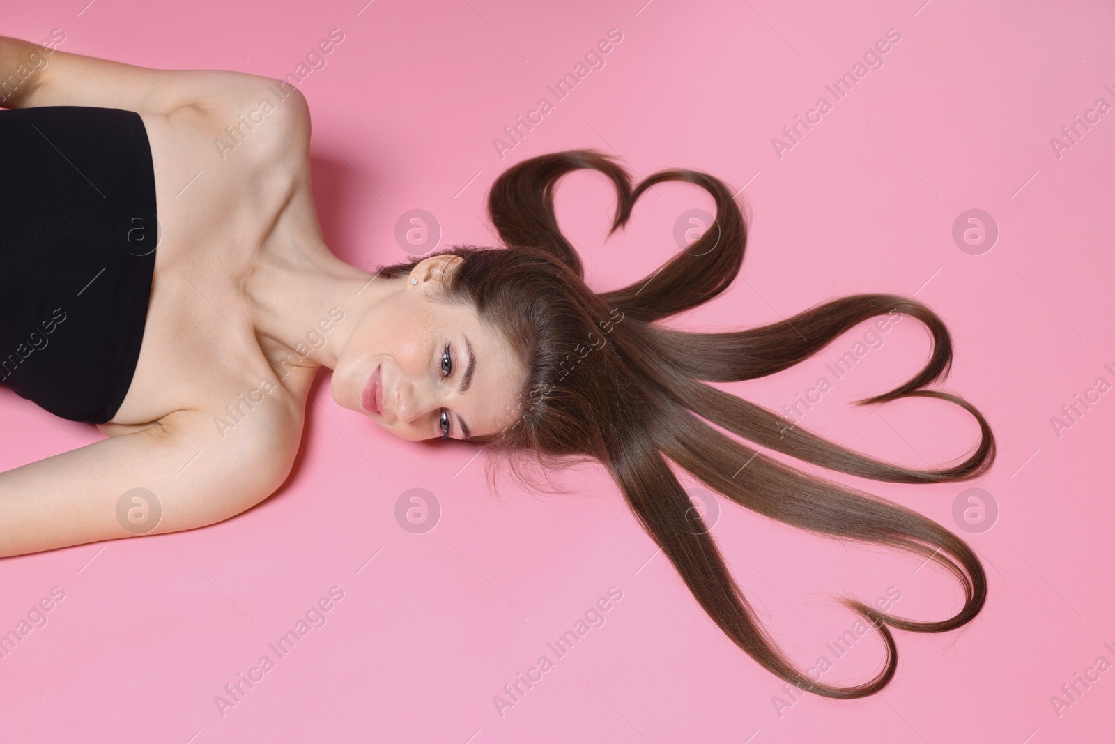 Photo of Beautiful young woman with hair in shape of hearts on pink background