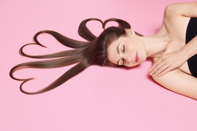 Photo of Beautiful young woman with hair in shape of hearts on pink background