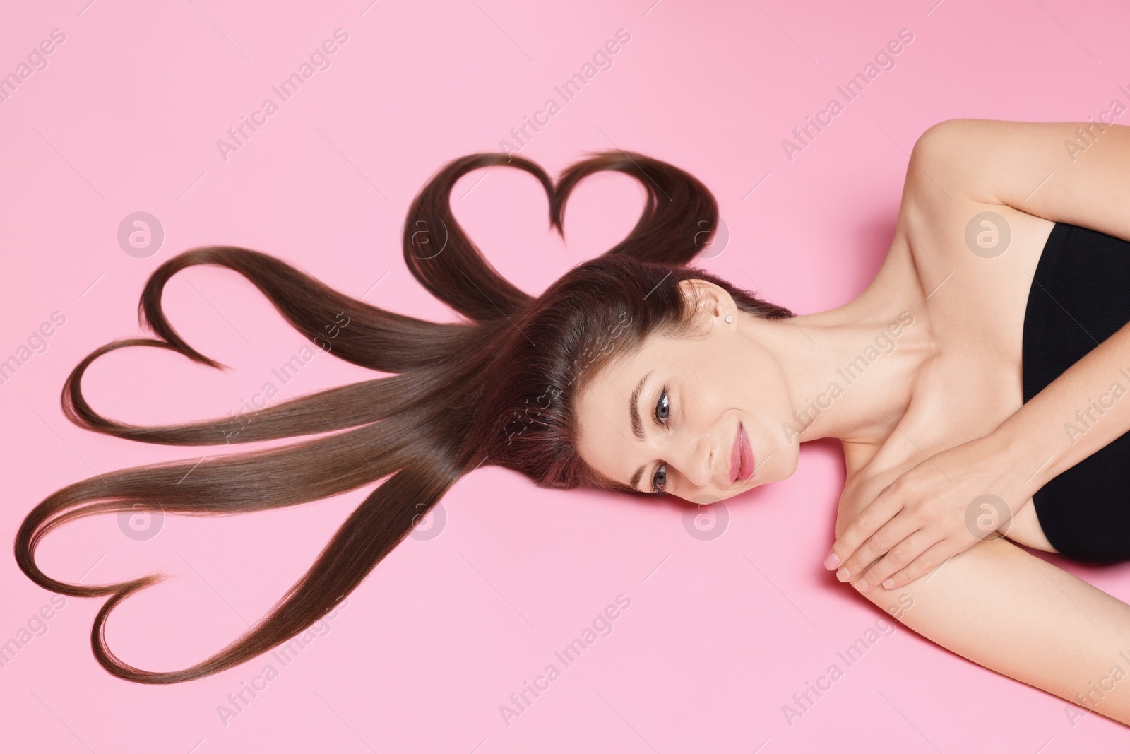 Photo of Beautiful young woman with hair in shape of hearts on pink background