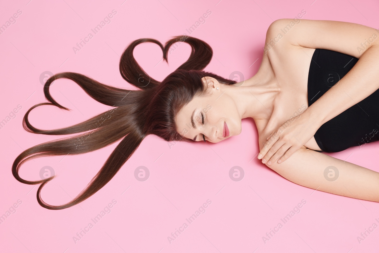 Photo of Beautiful young woman with hair in shape of hearts on pink background