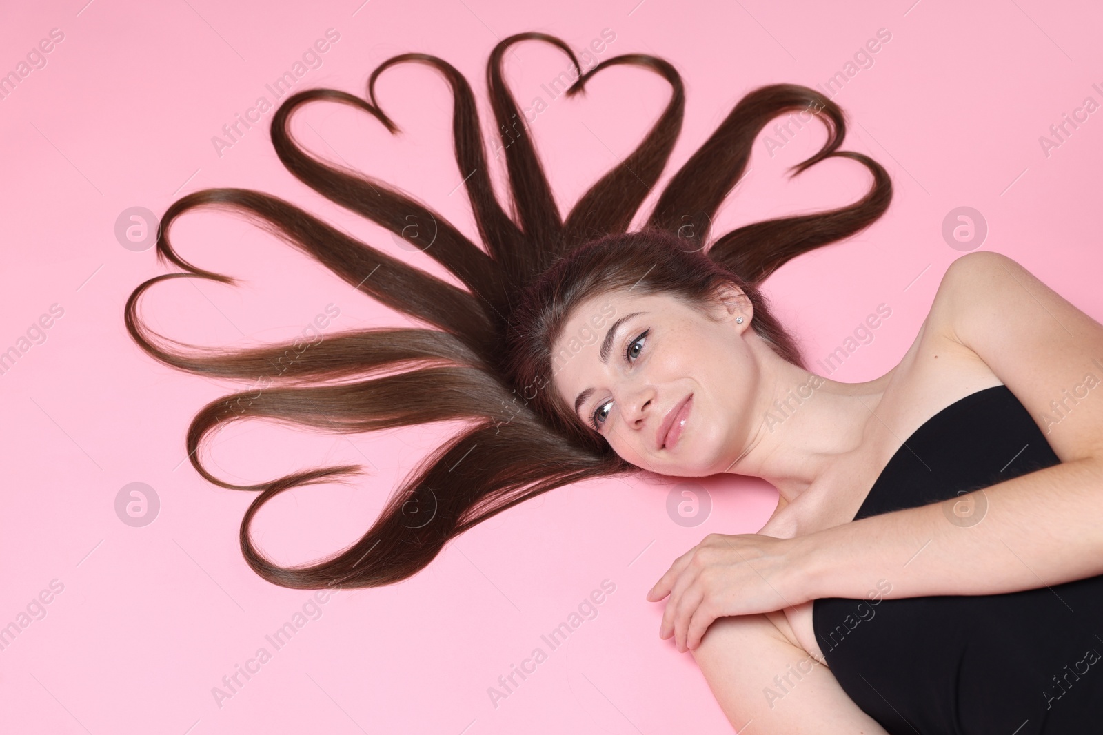 Photo of Beautiful young woman with hair in shape of hearts on pink background