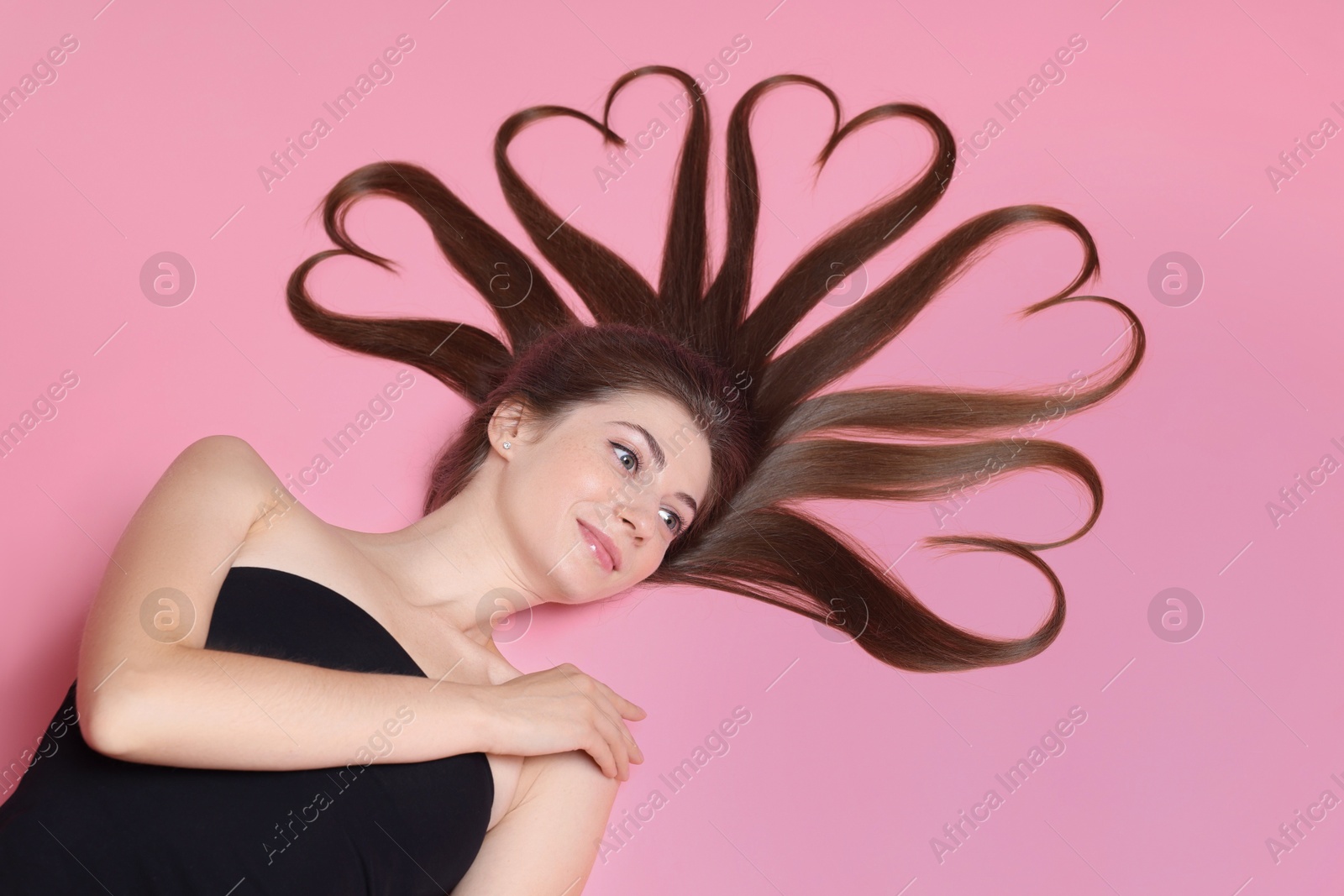 Photo of Beautiful young woman with hair in shape of hearts on pink background