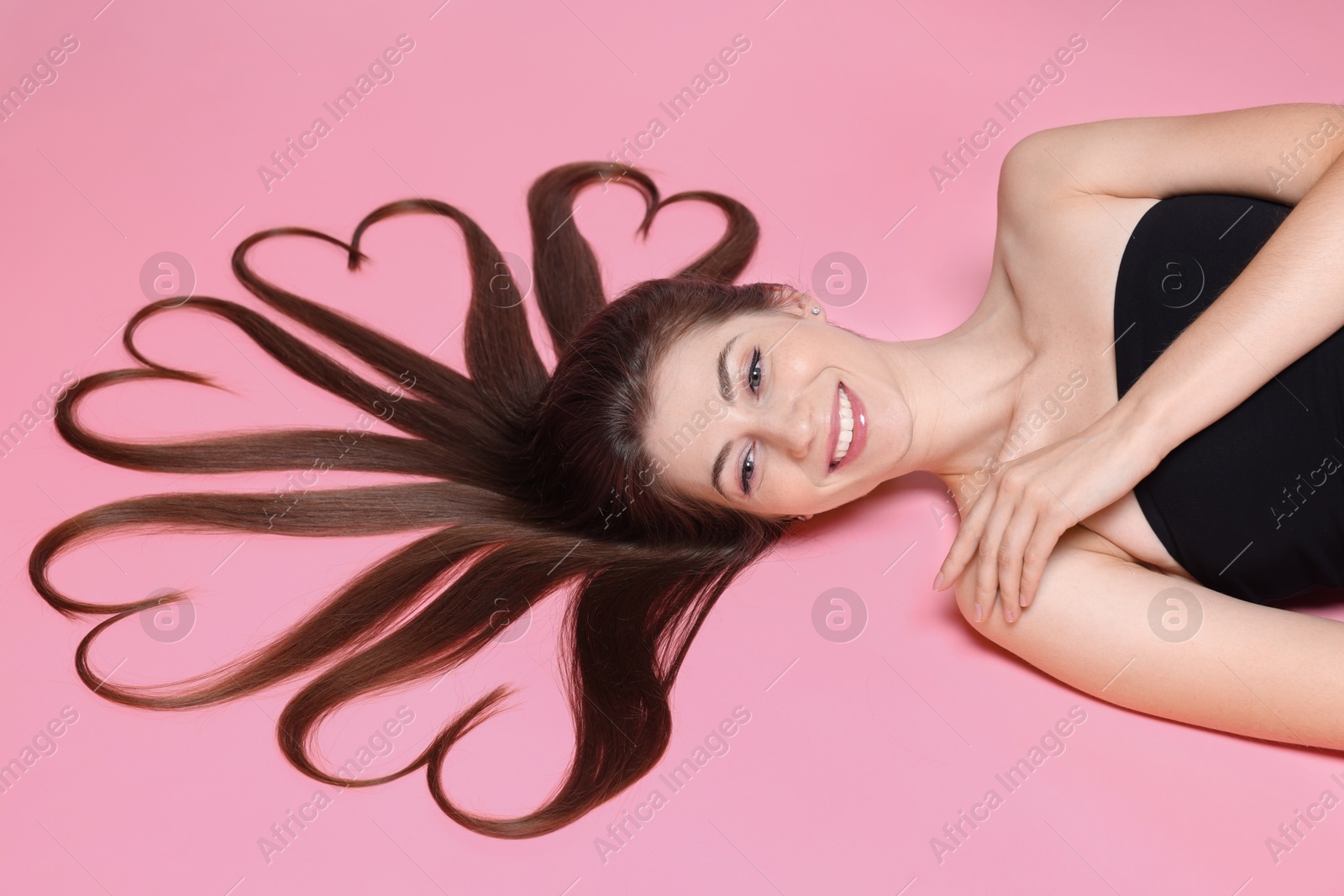 Photo of Beautiful young woman with hair in shape of hearts on pink background