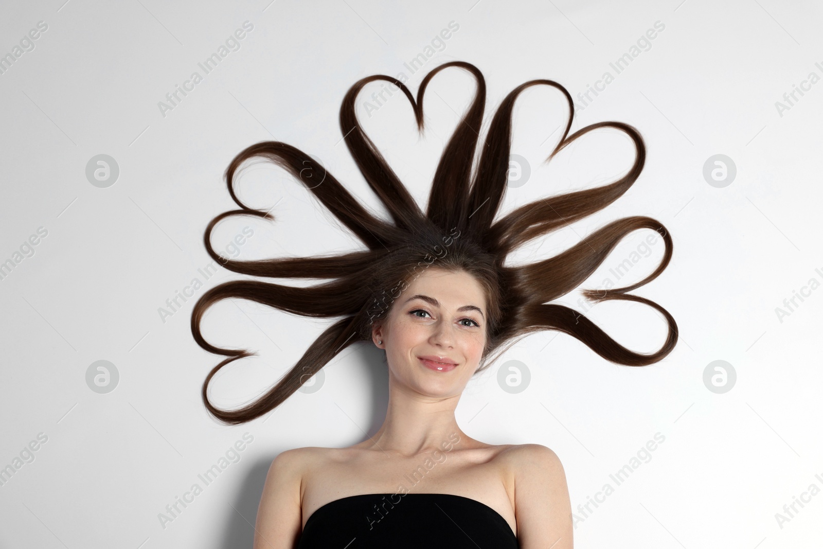 Photo of Beautiful young woman with hair in shape of hearts on white background, top view