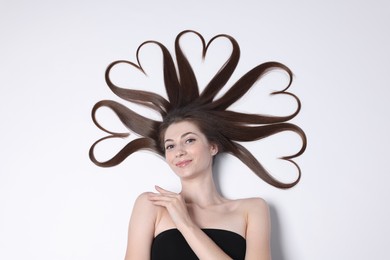 Photo of Beautiful young woman with hair in shape of hearts on white background, top view