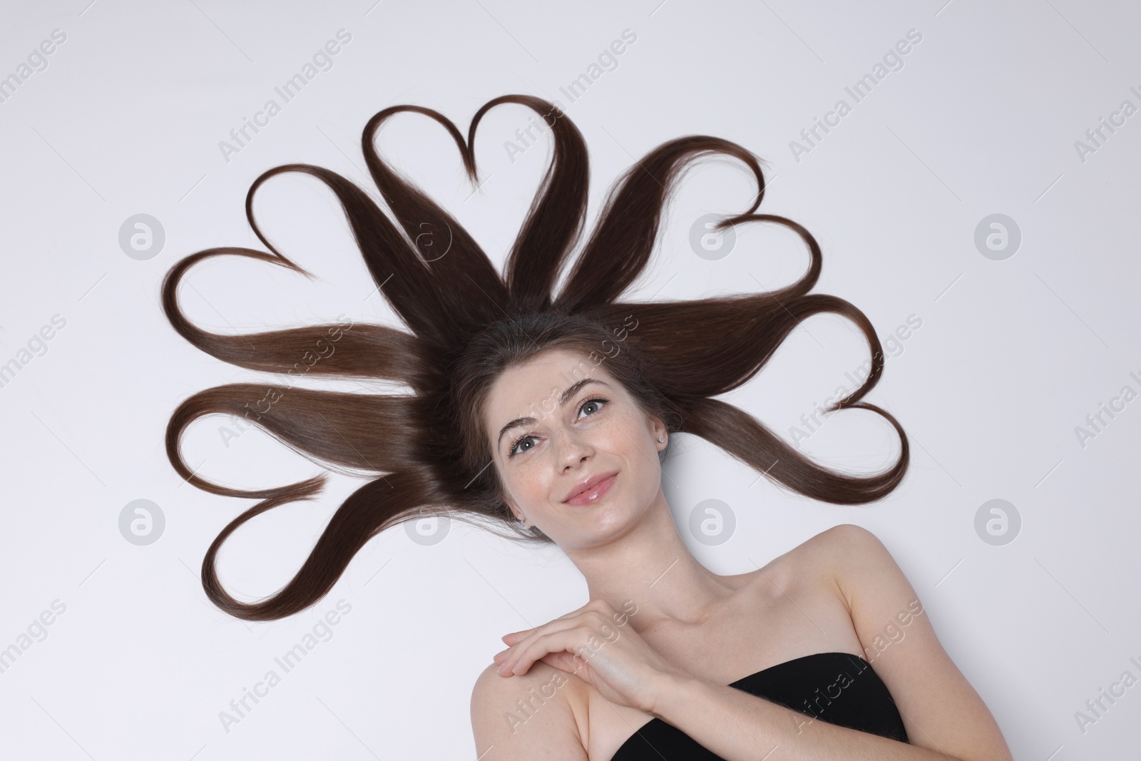 Photo of Beautiful young woman with hair in shape of hearts on white background, top view