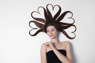 Photo of Beautiful young woman with hair in shape of hearts on white background, top view