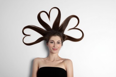 Beautiful young woman with hair in shape of hearts on white background, top view