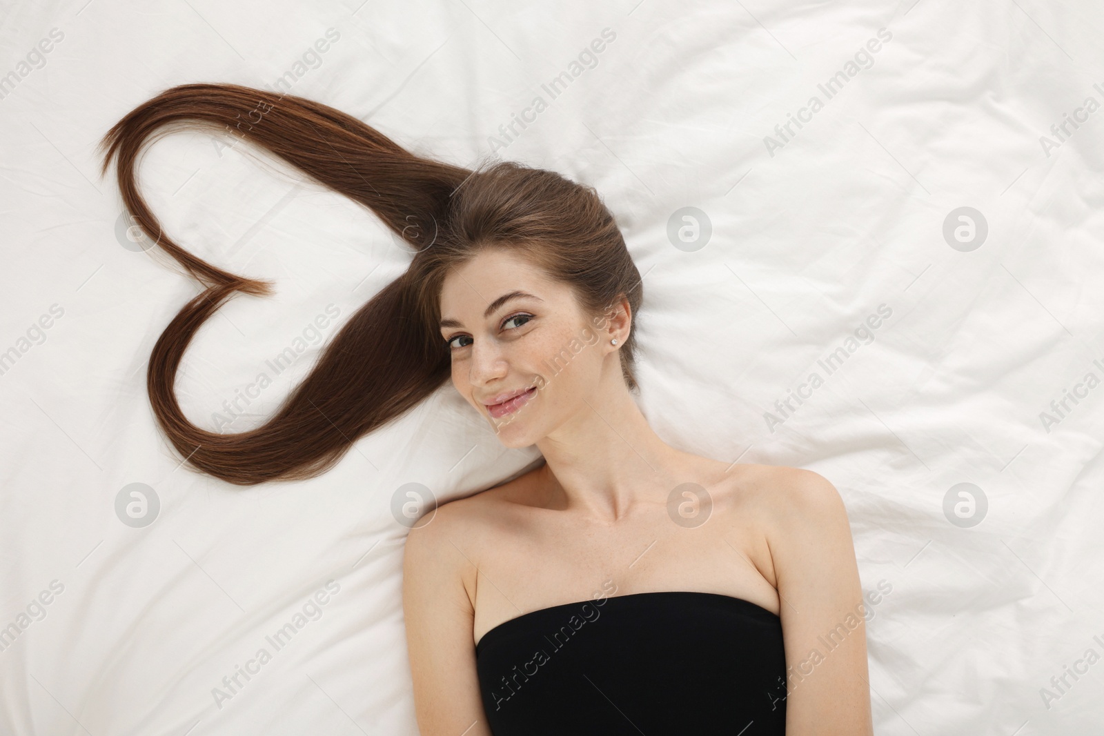 Photo of Beautiful young woman with hair in shape of heart on bed, top view