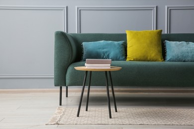 Stylish sofa with cushions and books on coffee table in room