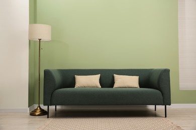 Photo of Stylish sofa with pillows and lamp near green wall indoors