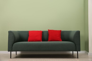 Photo of Stylish sofa with pillows near green wall indoors