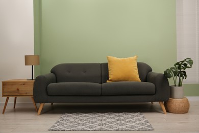 Stylish sofa with pillow, side table and houseplant near green wall indoors