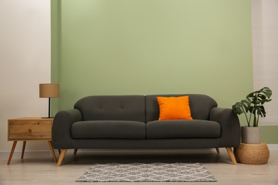 Stylish sofa with pillow, side table and houseplant near green wall indoors