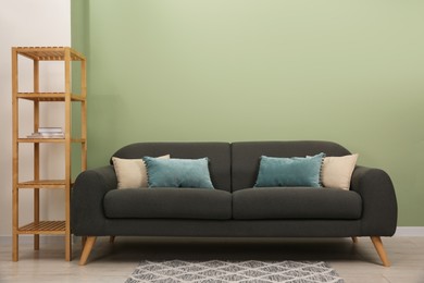 Stylish sofa with pillows and shelving unit near green wall indoors