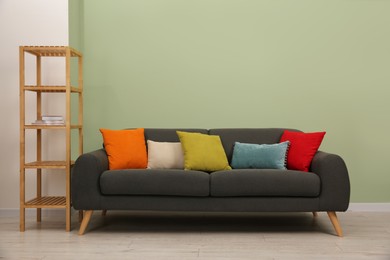 Stylish sofa with pillows and shelving unit near green wall indoors