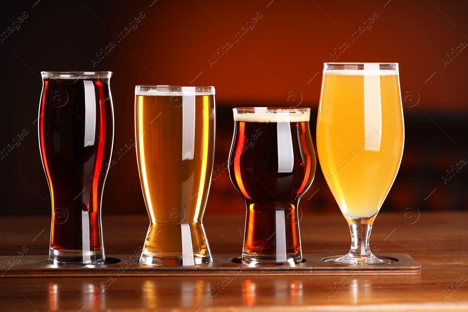 Photo of Glasses with different types of beer on wooden table against color background